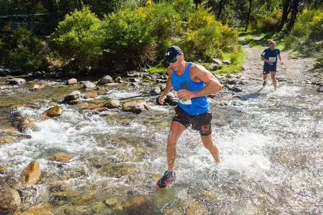 A man in a blue tank top is running through a river.