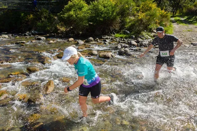 A man and a woman are running through a river.
