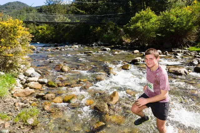 A man is standing in a river with a bridge in the background.