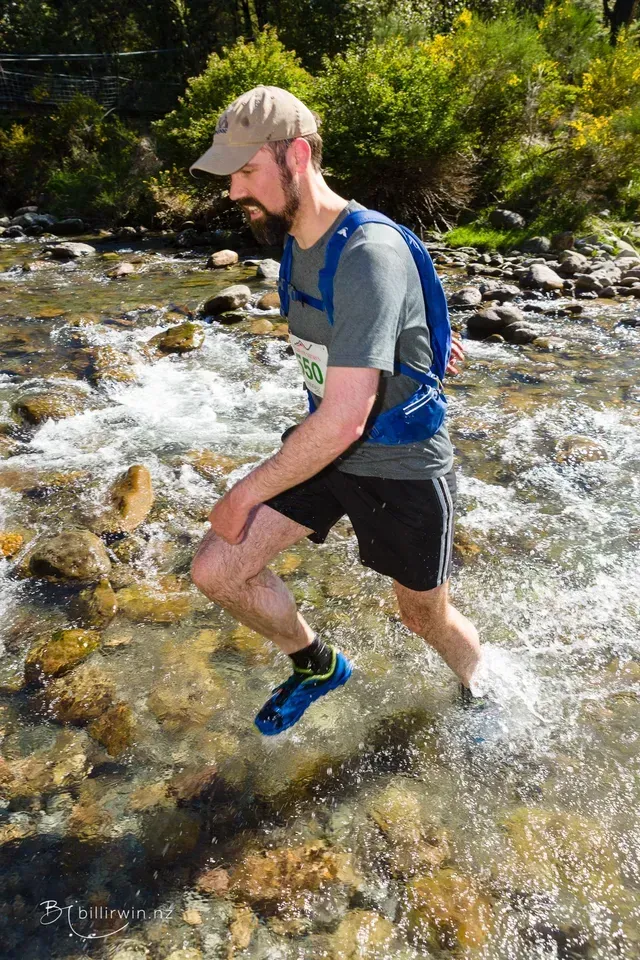 A man with a backpack is crossing a river.