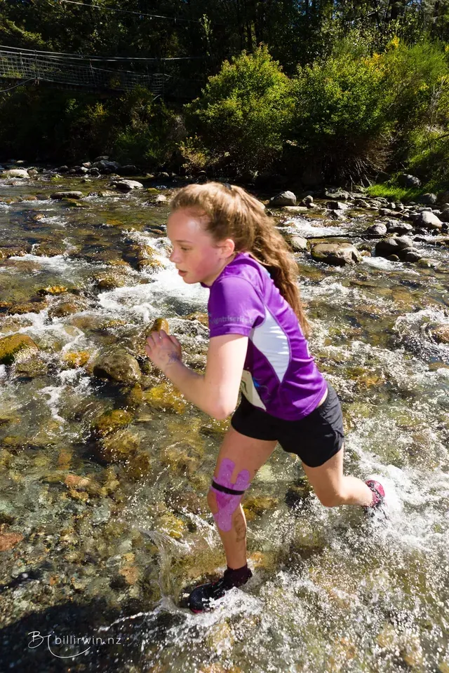 A woman in a purple shirt is running through a river.