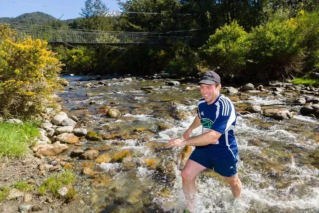 A man in a blue shirt is walking through a river.