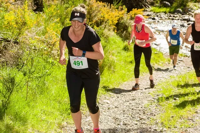 A group of women are running a trail in the woods.