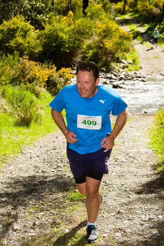 A man wearing a blue shirt with the number 499 on it is running down a dirt path.