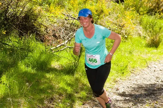 A woman is running on a trail in the woods.