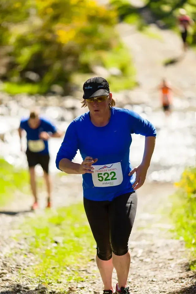 A woman in a blue shirt is running down a dirt path.