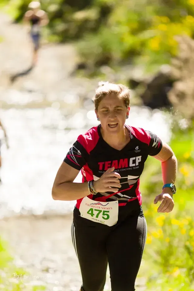 A woman in a team cp shirt is running down a trail.