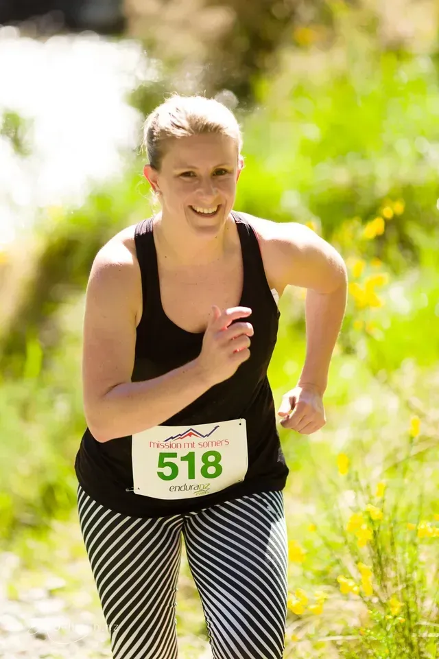 A woman in a black tank top and striped pants is running in a race.