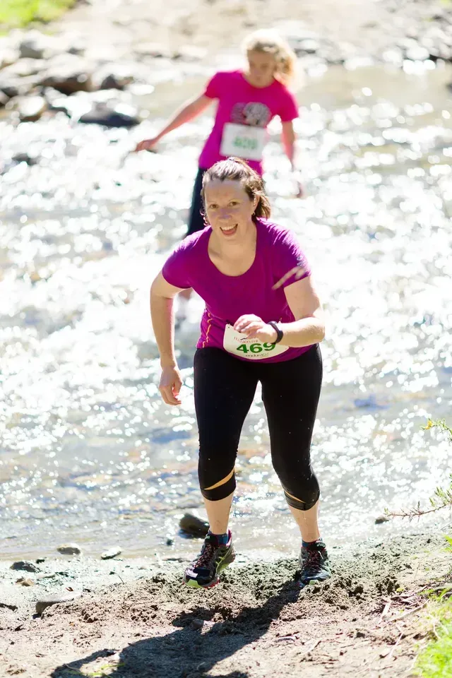 A woman in a purple shirt is running through a stream.