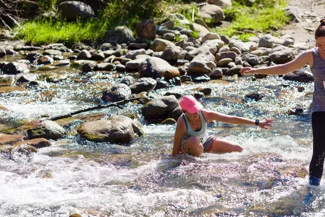 Two women are walking through a stream of water.