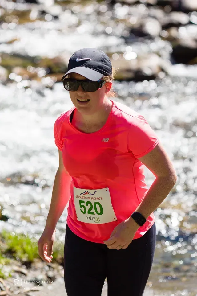 A woman in a pink shirt and black pants is running in a river.