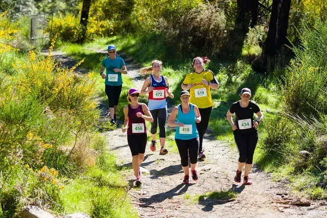 A group of women are running on a trail in the woods.