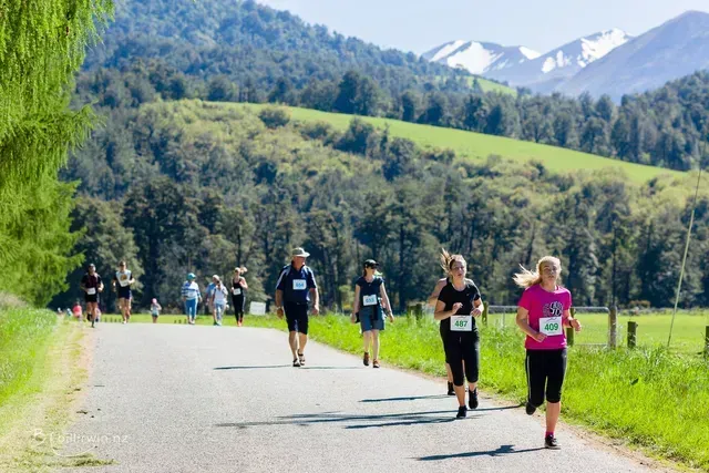 A group of people are running down a road with mountains in the background.