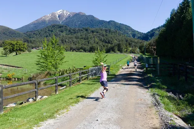 A woman is running down a dirt road with a mountain in the background.