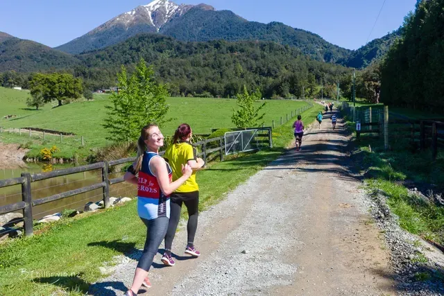Two women are running down a dirt road in the countryside.