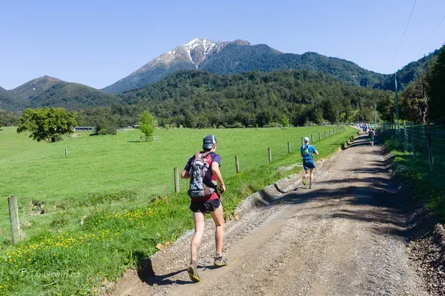 Two people are running down a dirt road in the mountains.