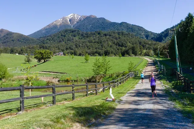 A woman is walking down a dirt road with a mountain in the background.