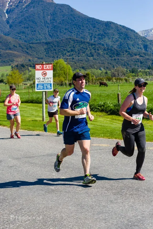 A group of people are running down a road in front of a no exit sign.