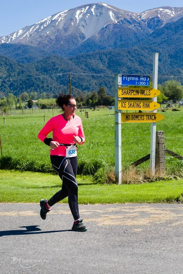 A woman is running down a road with mountains in the background.