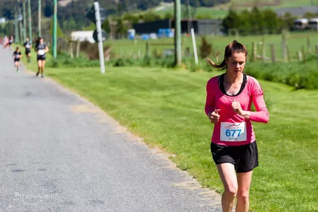 A woman in a pink shirt is running down a road.