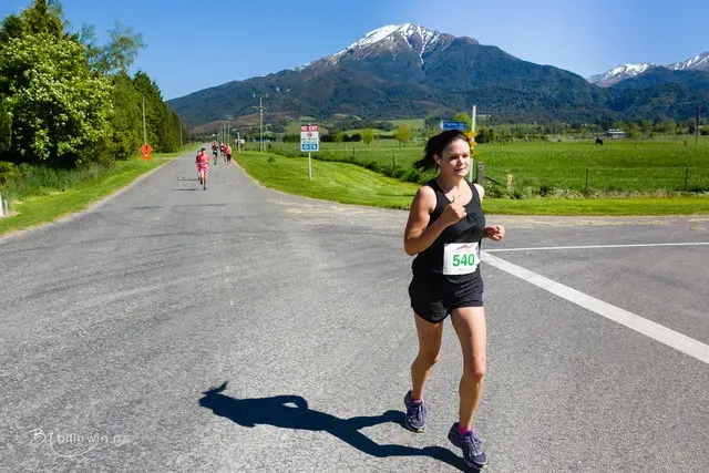 A woman is running down a road with a mountain in the background.