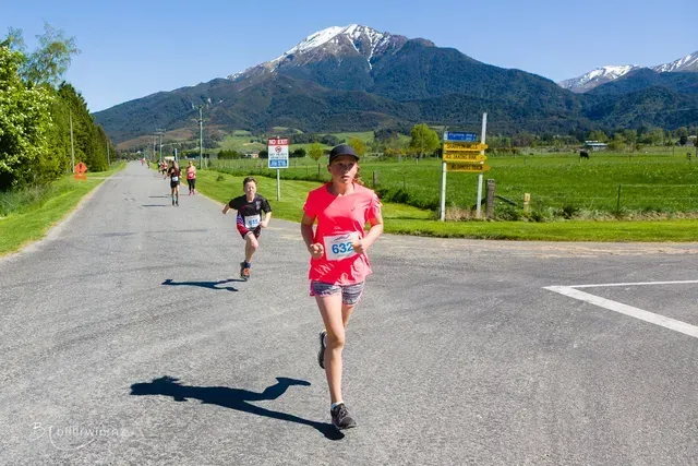 A group of people are running down a road with mountains in the background.