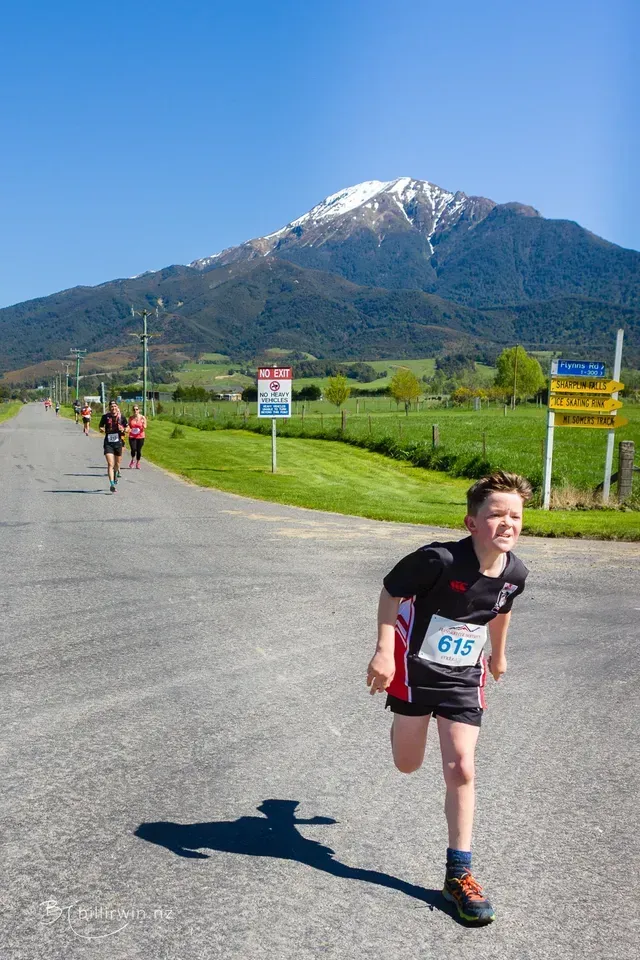 A young boy is running down a road with a mountain in the background.