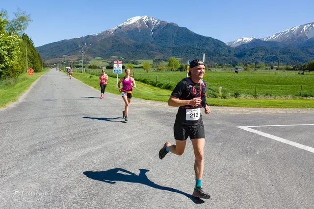 A group of people are running down a road with mountains in the background.
