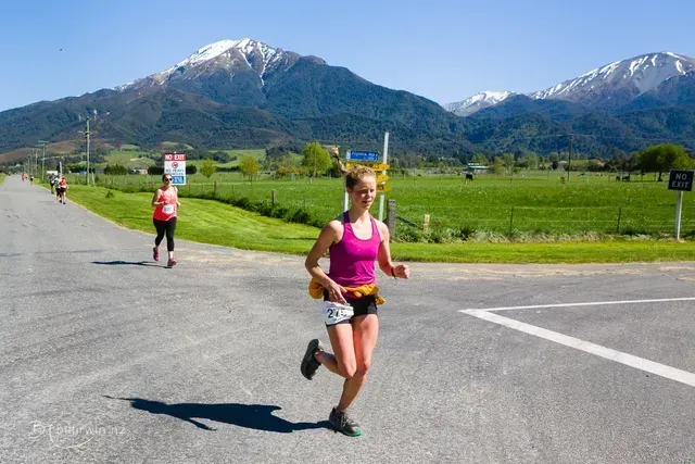 A woman is running down a road with mountains in the background.