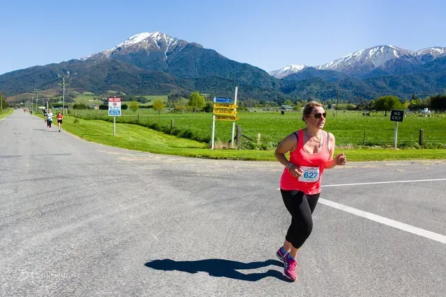 A woman is running down a road with mountains in the background.