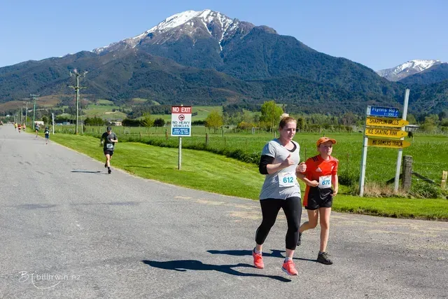 Two people are running down a road with mountains in the background.