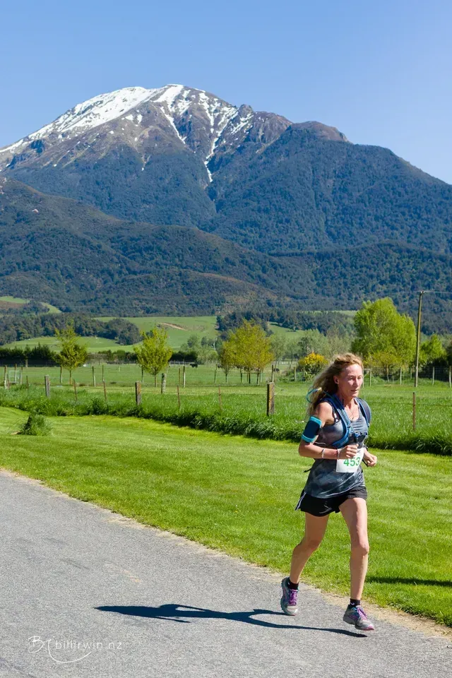A woman is running down a road with a mountain in the background.