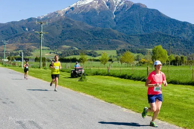 A group of people are running down a road in front of a mountain.
