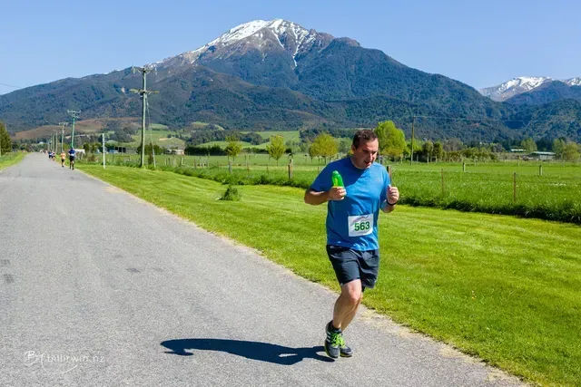 A man is running down a road with a mountain in the background.