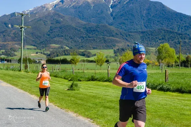 A man and a woman are running down a road in front of a mountain.