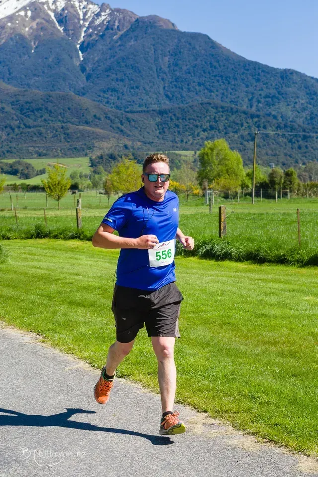 A man is running down a road with mountains in the background.