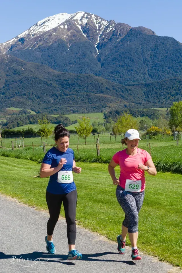Two women are running on a path with a mountain in the background.