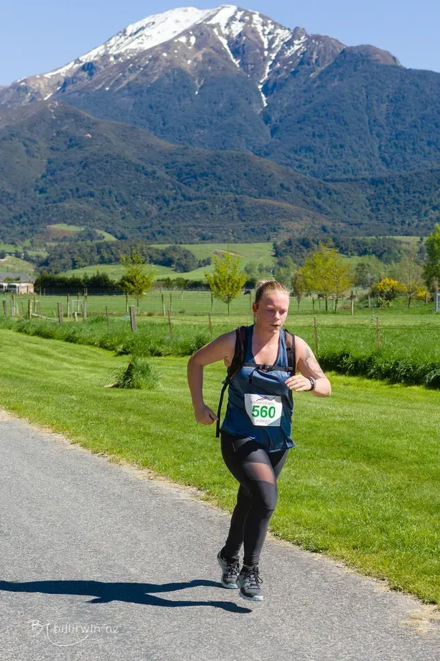 A woman is running down a road with a mountain in the background.