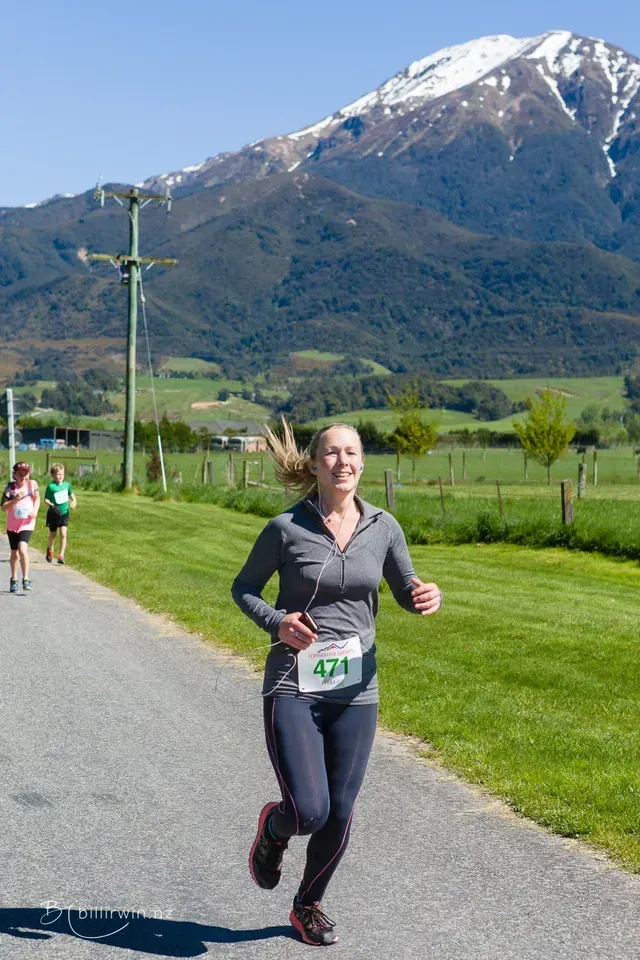A woman is running down a road with a mountain in the background.