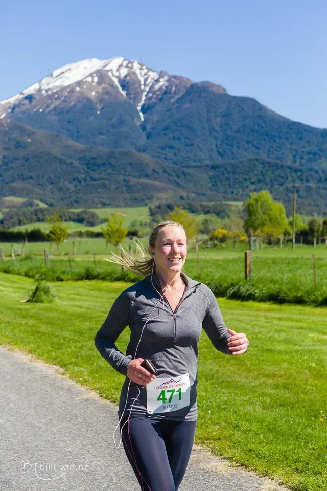 A woman is running on a road with a mountain in the background.