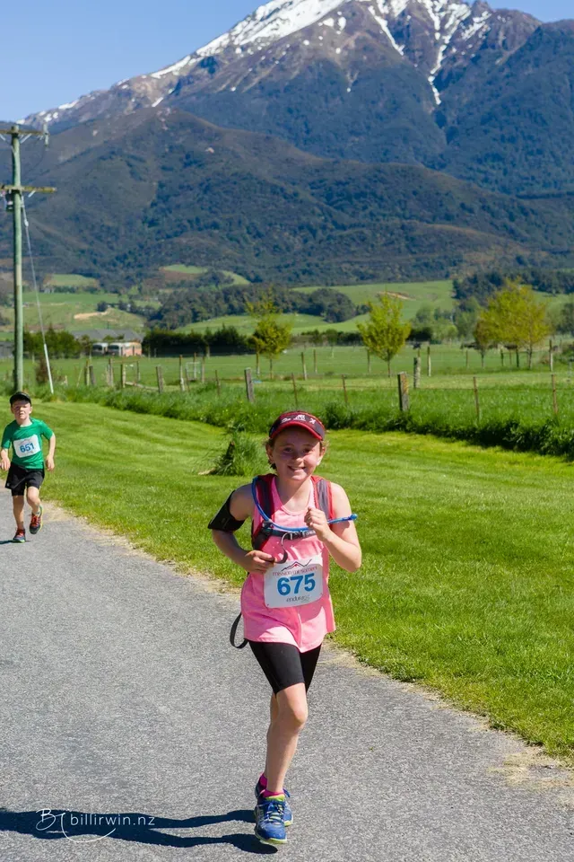 A young girl is running down a road with a mountain in the background.