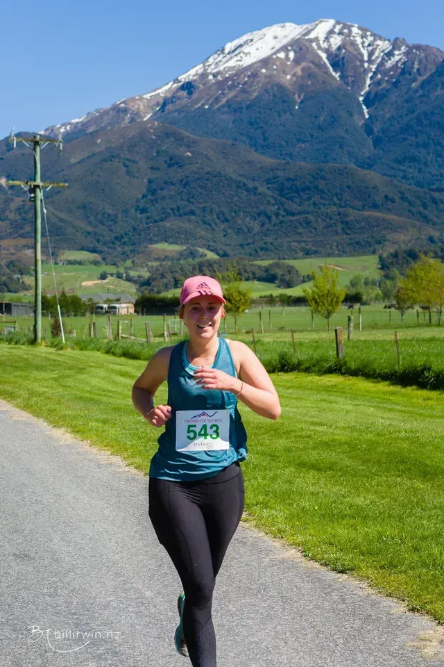 A woman is running down a road with a mountain in the background.