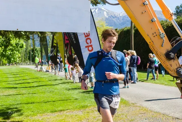 A man is running in front of a large yellow excavator.