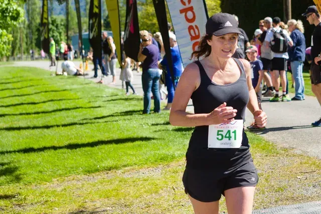 A woman in a black tank top and shorts is running in a park.