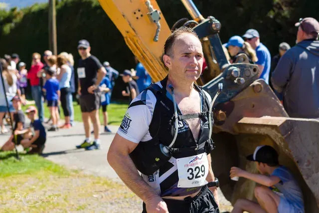 A man with the number 329 on his shirt is standing in front of a large excavator.