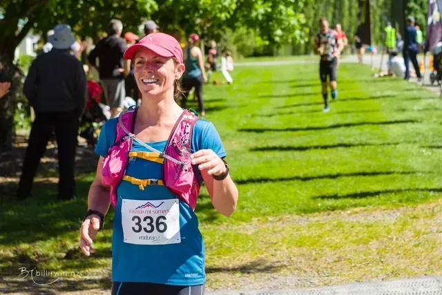 A woman wearing a pink hat and a blue shirt is standing in a grassy field.