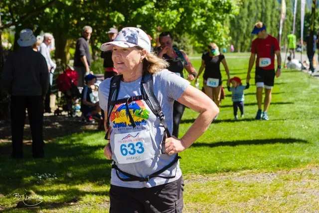 A woman is running in a park with a number 633 on her shirt.