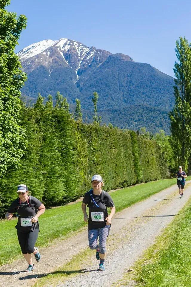 Two people are running down a dirt road with a mountain in the background.