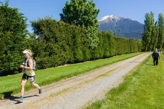 A woman is running down a dirt road with a mountain in the background.