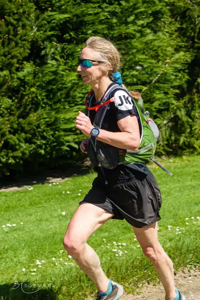 A woman is running on a trail with a backpack.